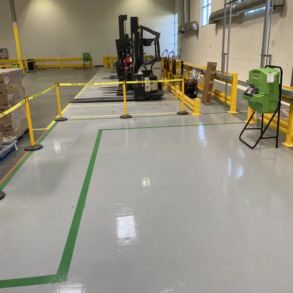 Warehouse floor in gray epoxy with green walkway striping, yellow guard rails and a forklift