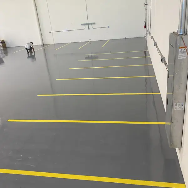 Gray epoxy warehouse floor with yellow aisle lines and a worker at the far end