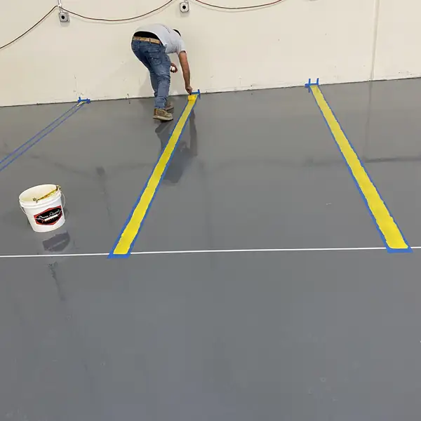 Worker taping out a yellow safety line on a freshly coated gray epoxy floor
