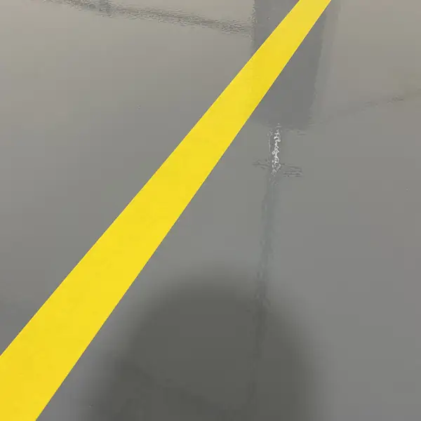 Yellow safety stripe running diagonally across a gray epoxy floor