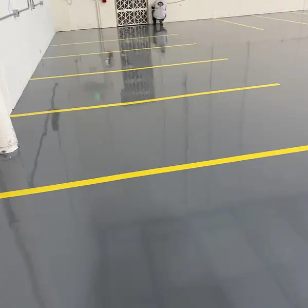 Gray epoxy warehouse floor with yellow striping and a worker in the distance