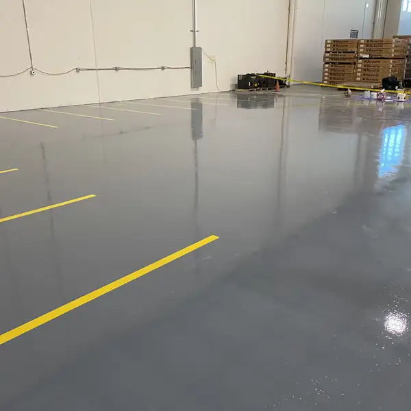 Gray epoxy floor with yellow lines leading toward stacked warehouse pallets