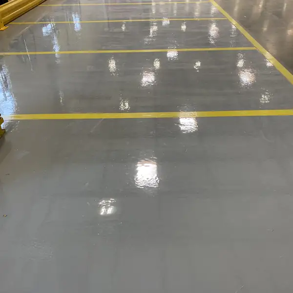 High-gloss gray epoxy warehouse floor reflecting the overhead lights between yellow lines