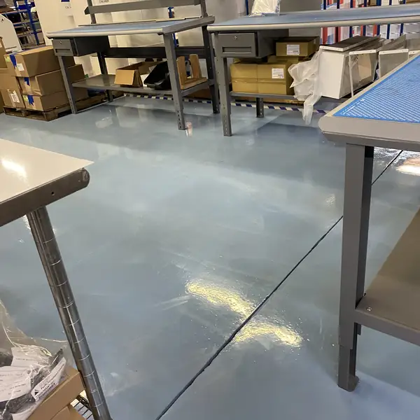 Pale blue epoxy floor beneath stainless workbenches in a production area
