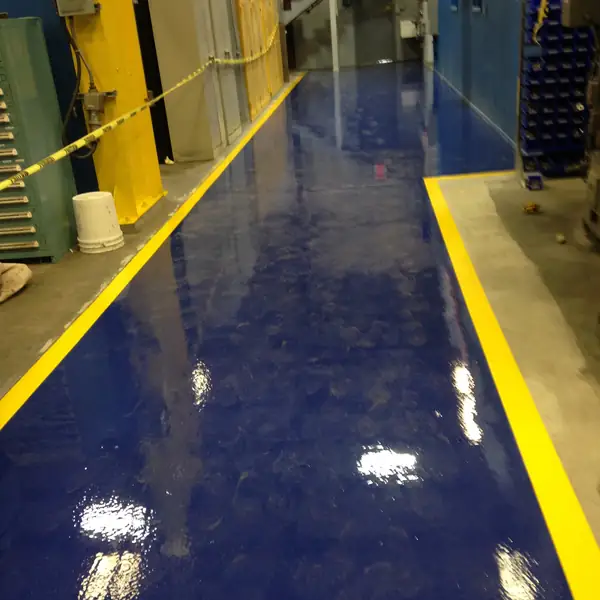 Deep blue epoxy floor with yellow safety lines running through a plant