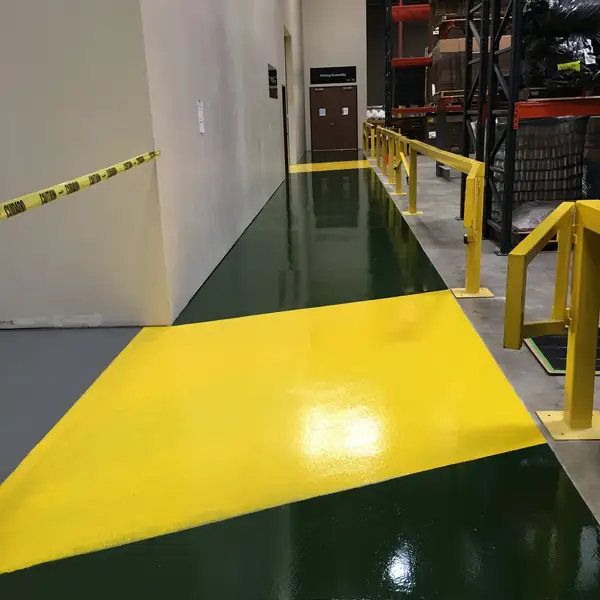 Green and yellow epoxy walkway meeting gray floor coating beside yellow guard rails