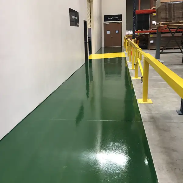 Green epoxy walkway running beside a yellow safety rail in a warehouse