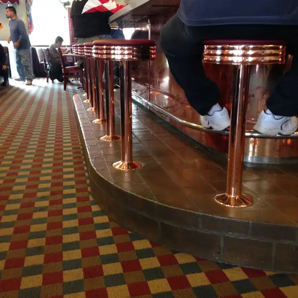 Diner counter with copper stools standing on a red and gold checcurboard floor overlay