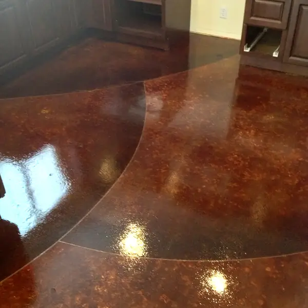 Dark red stained concrete floor curving into a kitchen