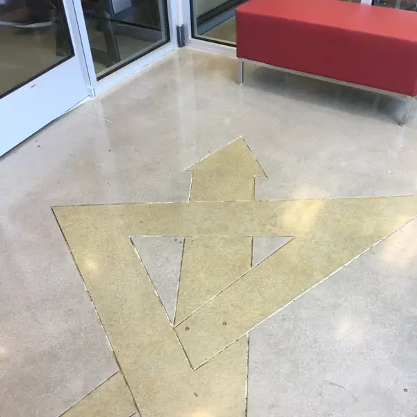 Gold stained arrow and triangle graphic in a polished floor beside a red bench