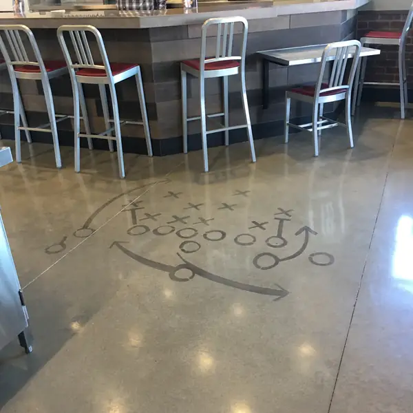 Football play diagram cut into a polished concrete floor beside a servery counter