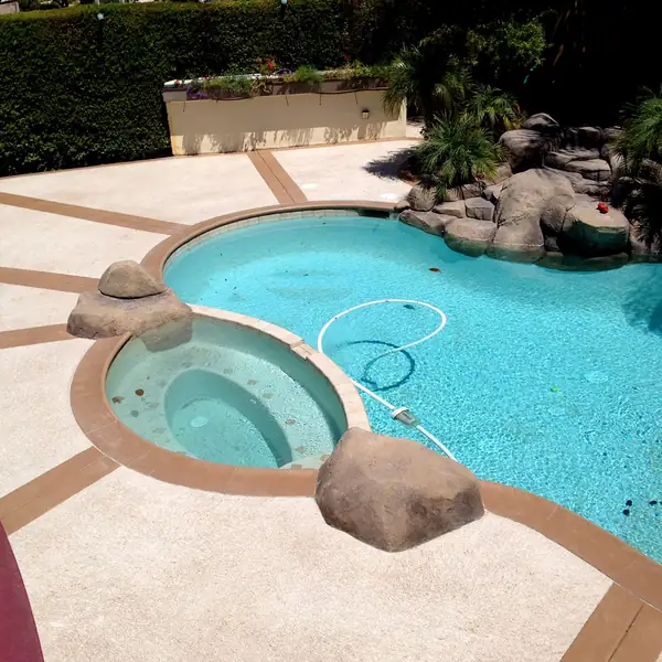 Backyard pool and raised spa surrounded by a tan textured cool deck