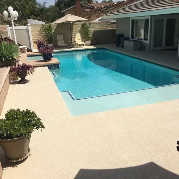 Curved backyard pool with a cream textured deck, fire pit and hillside view