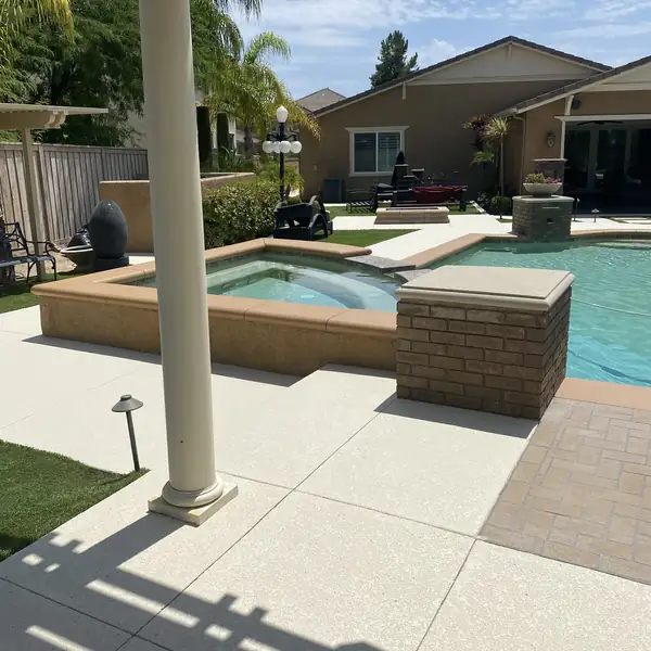 Pool and spa seen from a covered patio with a cream textured deck