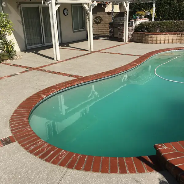 Kidney-shaped pool with red brick coping and a light gray textured deck