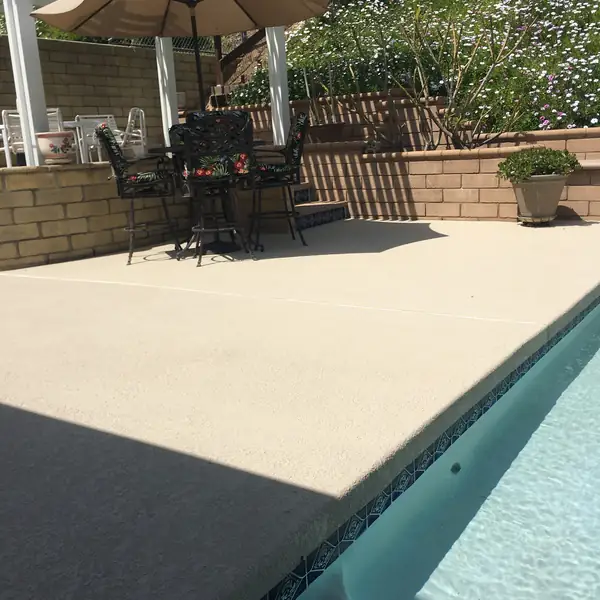 Patio furniture and umbrellas on a cream pool deck beside a backyard pool