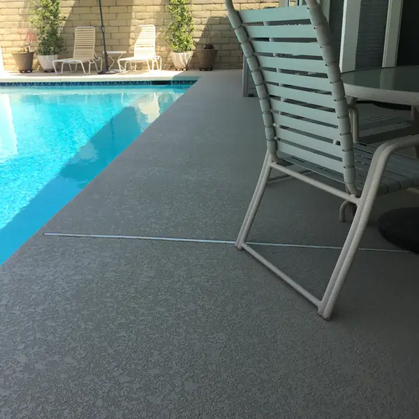 Poolside chairs on a gray textured deck beside clear blue water
