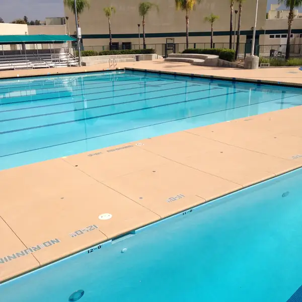 Commercial lap pool with a wide tan textured deck and stainless handrails