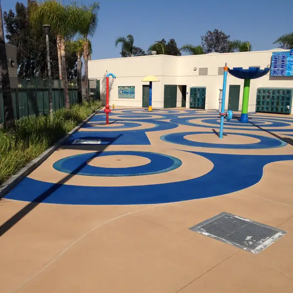 Blue swirl splash pad set into a tan deck outside a community building
