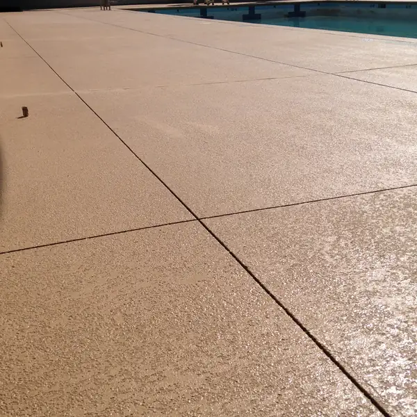 Wide tan textured pool deck running to the water's edge