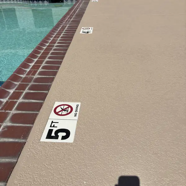 Tan pool deck with a five foot depth marker beside red brick coping