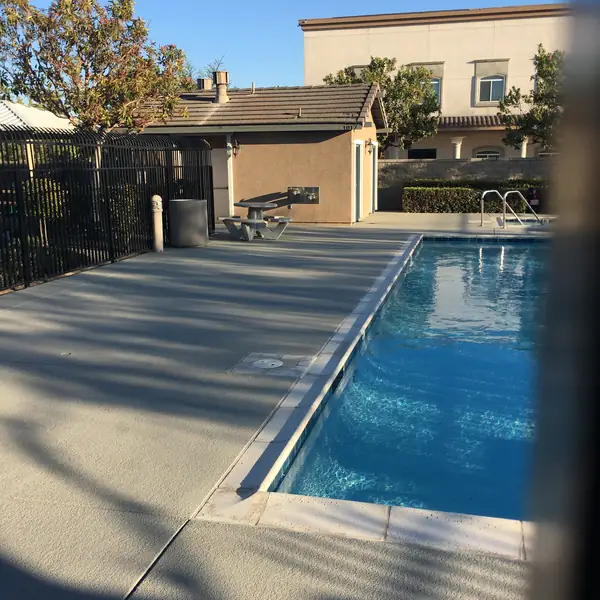 Backyard pool with a gray textured deck behind a wrought iron fence