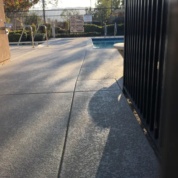 Gray speckled pool deck seen past a black metal fence