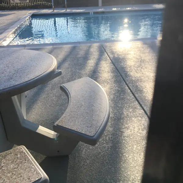 Concrete table and benches on a speckled gray pool deck