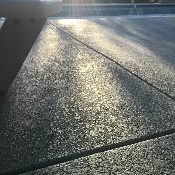 Textured gray deck lit by low sun beside a pool