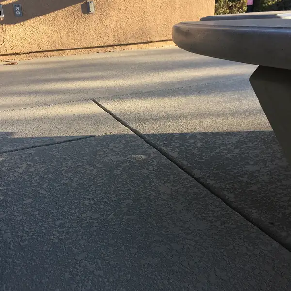 Gray textured pool deck with a concrete table at the edge of frame