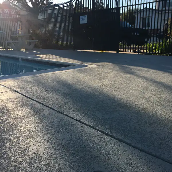 Gray textured pool deck behind a black fence at a community pool