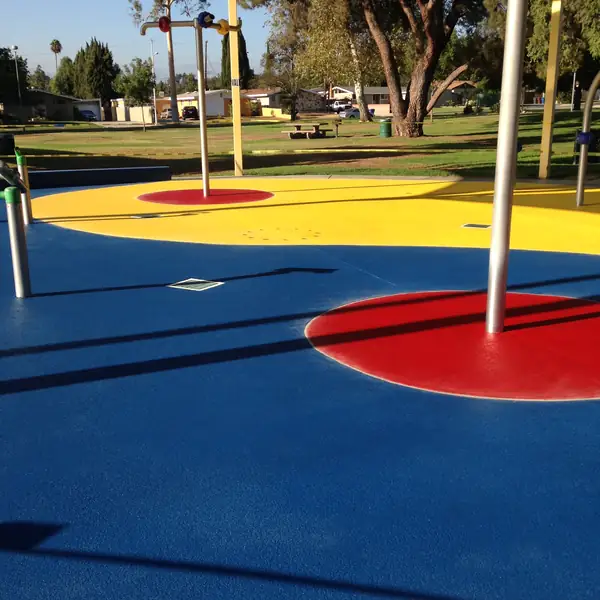 Blue and yellow splash pad in a park with a red circle and play posts