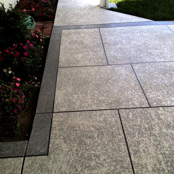 Gray textured walkway with a dark border running past flowering beds