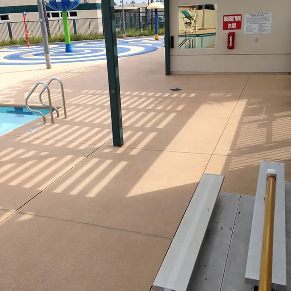 Tan pool deck running under a shade structure at a community pool