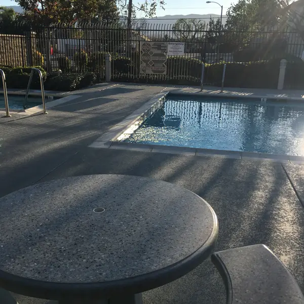 Concrete table and stools on a gray textured pool deck with a blue-gray border beside a community pool