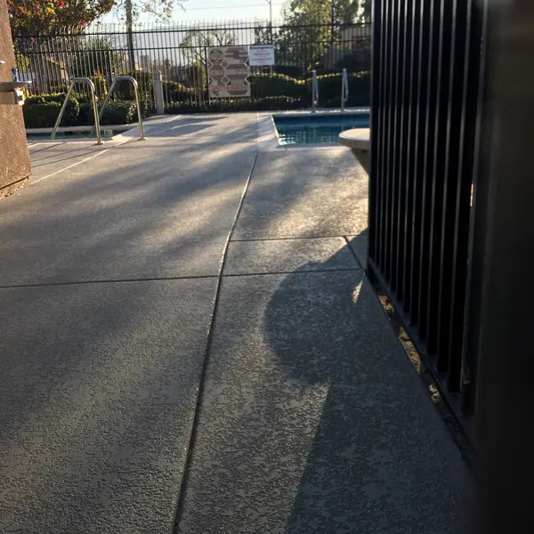Gray resurfaced walkway with a blue-gray edge band leading past a black fence to a pool
