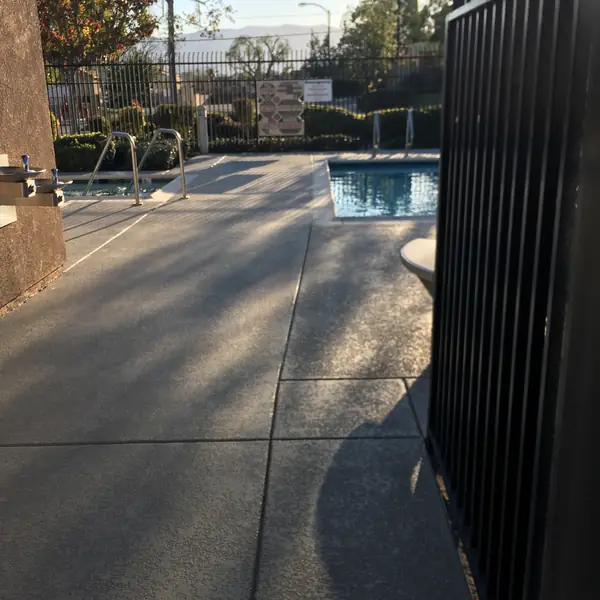 Gray textured pool deck with a dark blue-gray border seen from the gate