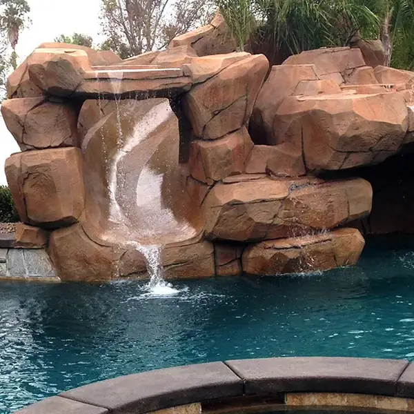 Terracotta faux rock waterfall feature above a clear blue pool