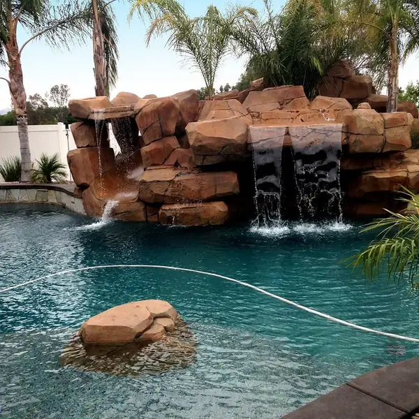 Rock waterfall with twin falls running into a pool framed by palms
