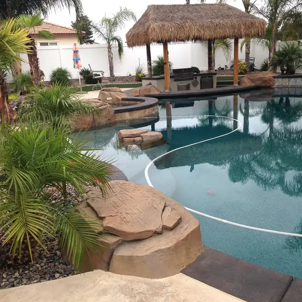 Backyard pool with restained boulders and a thatched palapa