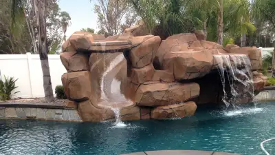 Stained faux-rock waterfall spilling into a turquoise pool on a Wildomar backyard deck